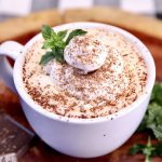 closeup of mug of hot chocolate with whipped cream, chocolate shavings and sprig of mint