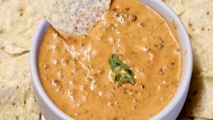 Chili Cheese Dip in a bowl with a tortilla chip dipping