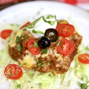 Burrito bake with ground beef and refried beans on a plate with sour cream, tomatoes, olives.