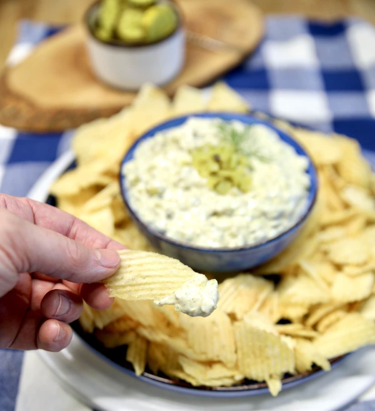 Creamy dip with pickles dipping with potato chips.