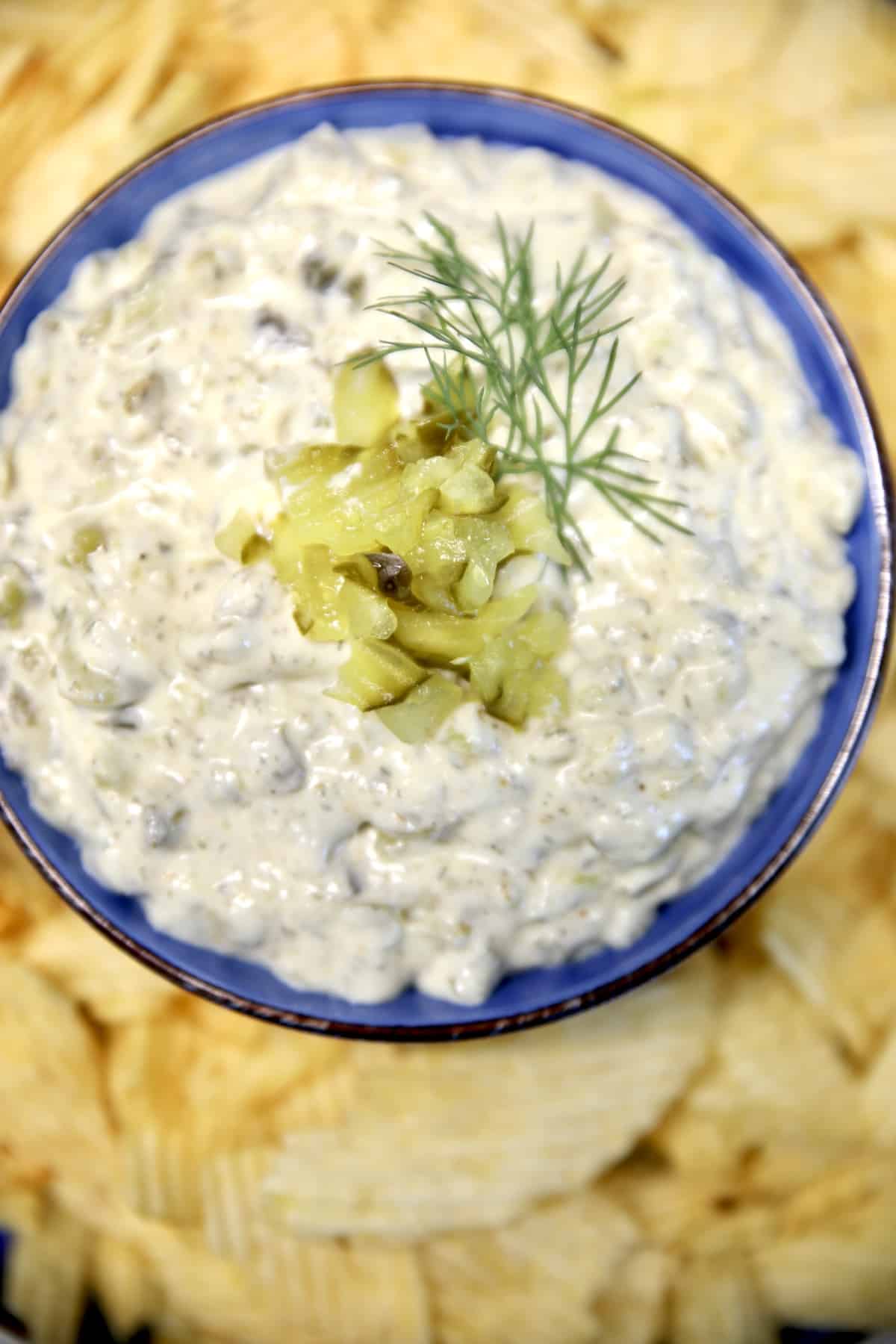 Bowl of pickle dip with dill garnish and potato chips.