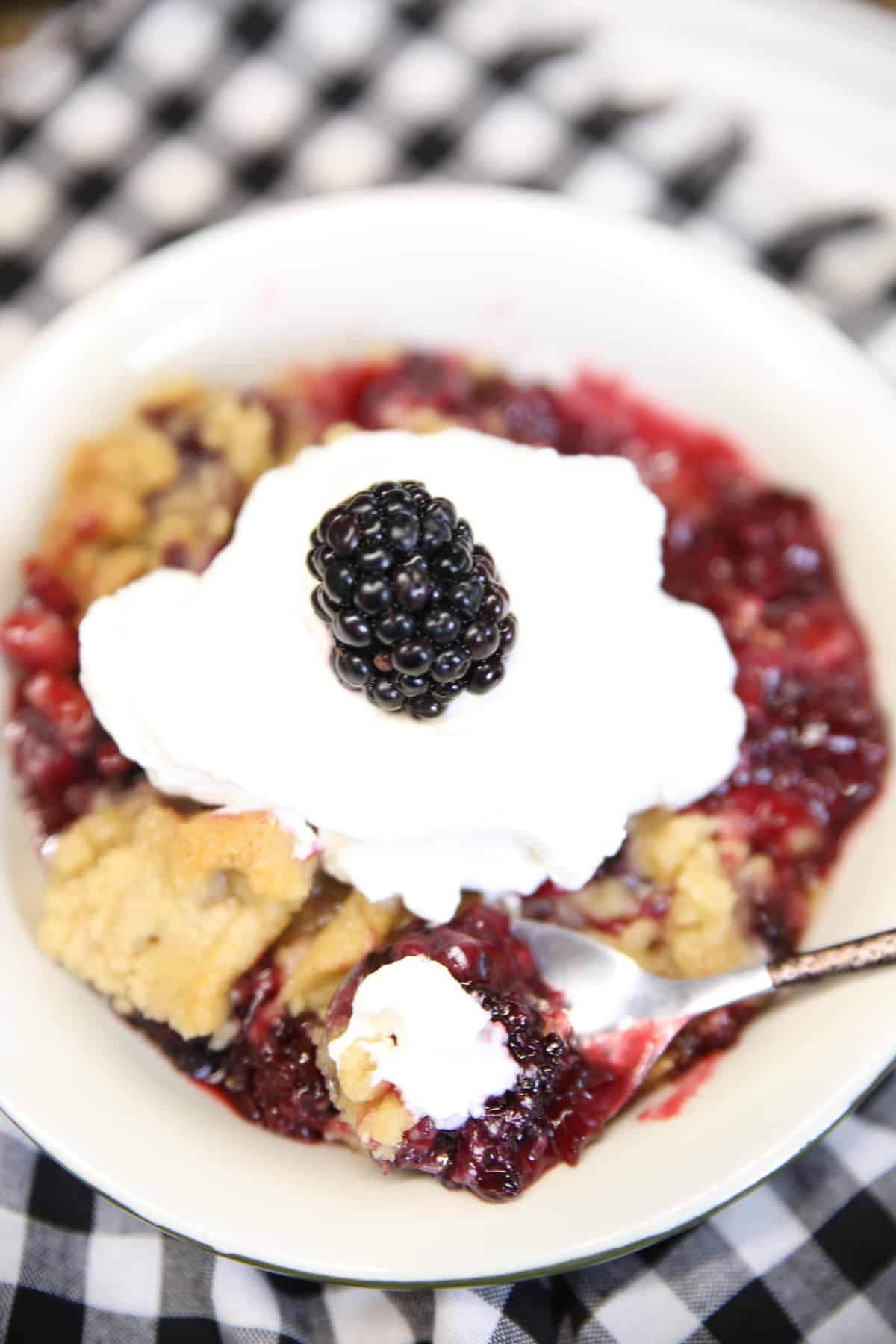 Bowl of blackberry crumble dessert with whipped cream - bite on a spoon.