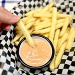 Dipping French fry into cup of fry sauce in a basket.