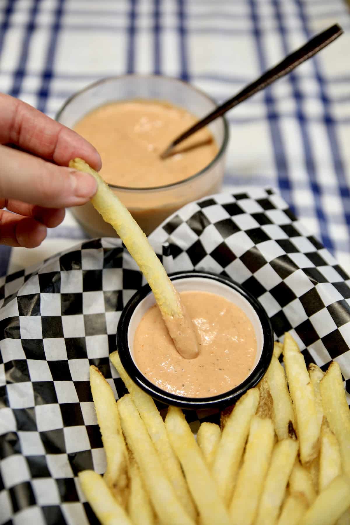 Basket of fries one dipping into sauce cup.