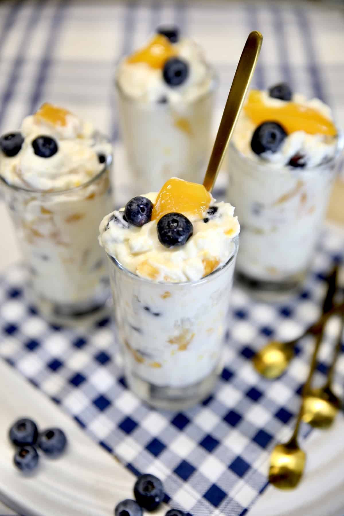 Glasses of no bake cheesecake with peaches and blueberries in glasses.