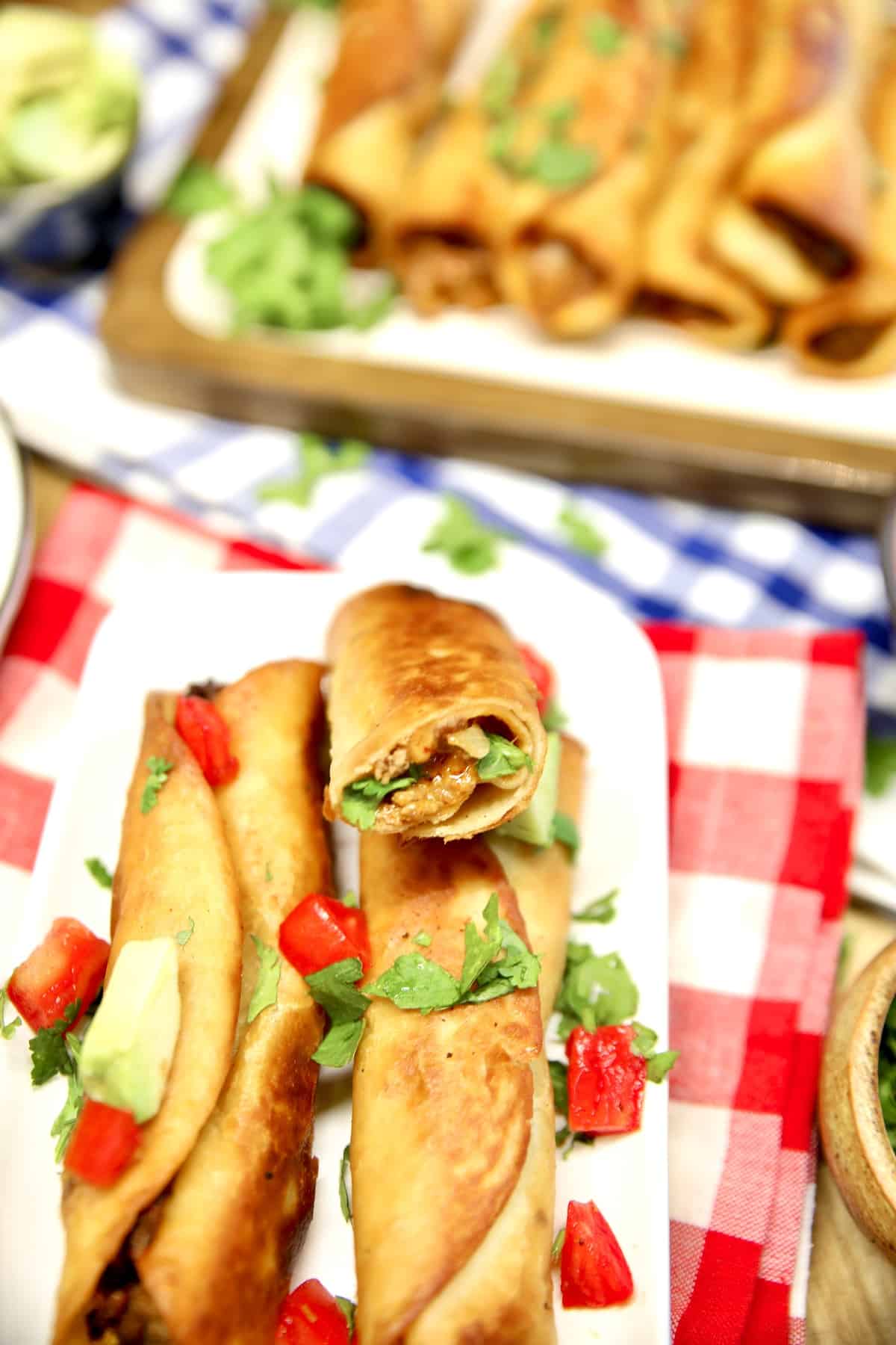 Cheesy chipotle beef taquitos on a platter, one cut in half.