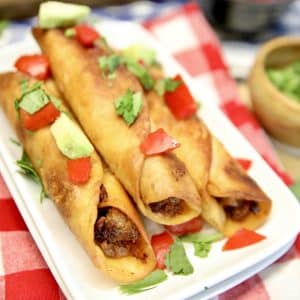 Chipotle Ground Beef Taquitos on a platter with tomatoes and avocado.