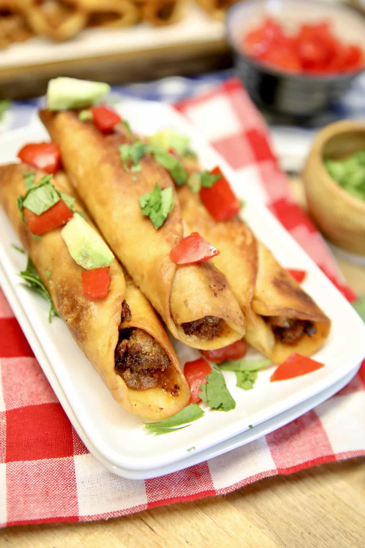 Taquitos on a plate with tomatoes and avocado.