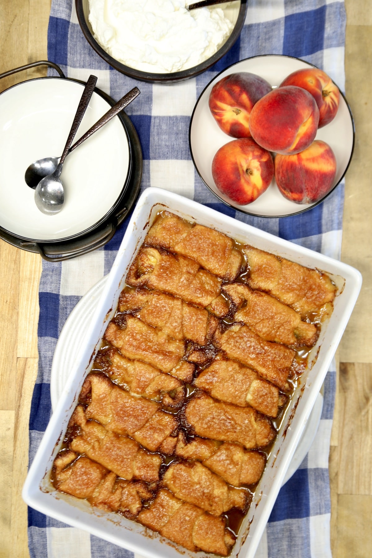 Peach dumplings in a pan with bowl of peaches, plates.