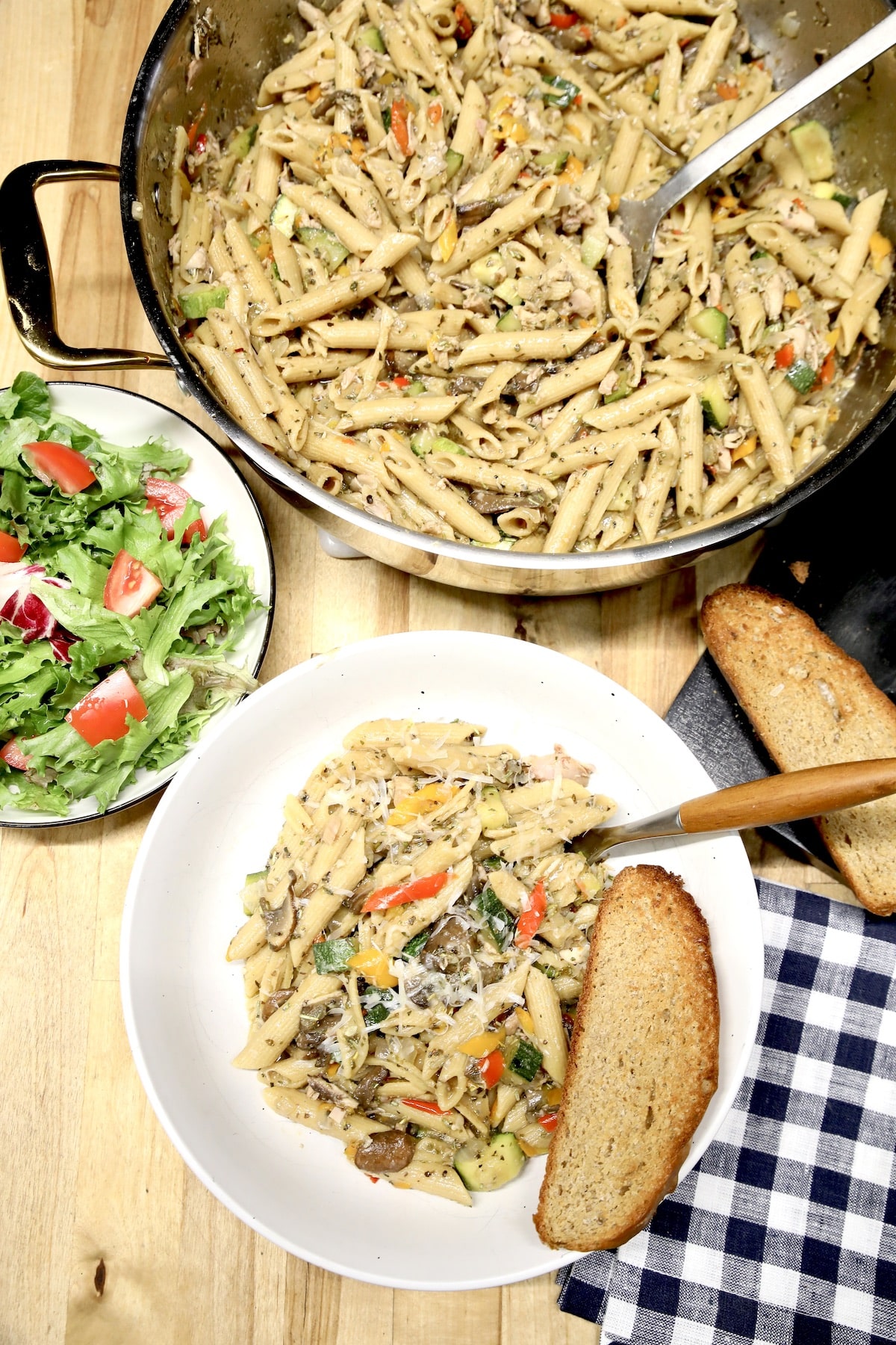 Pasta in a bowl with pan of pasta and salad. 