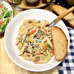 Bowl of pasta with vegetables and slice of bread.