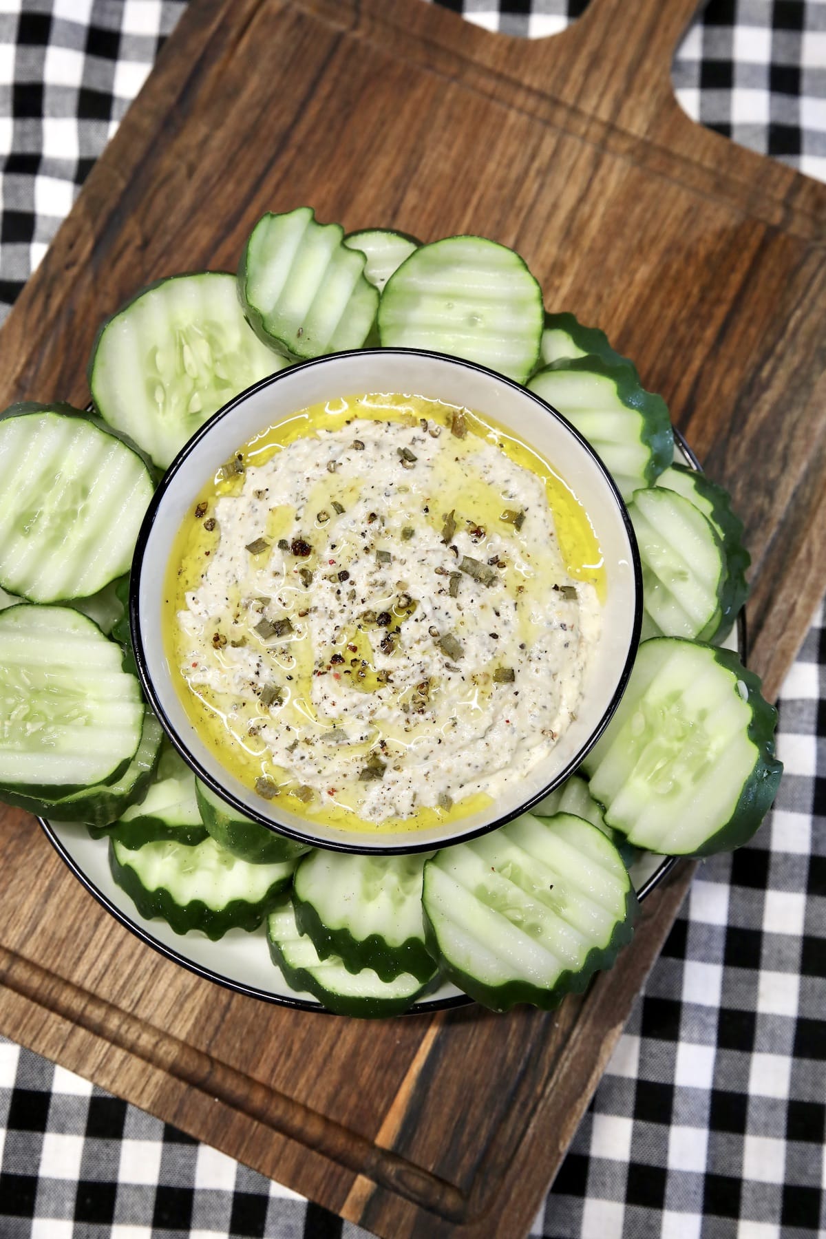 Board with cucumber slices and bowl of dip.