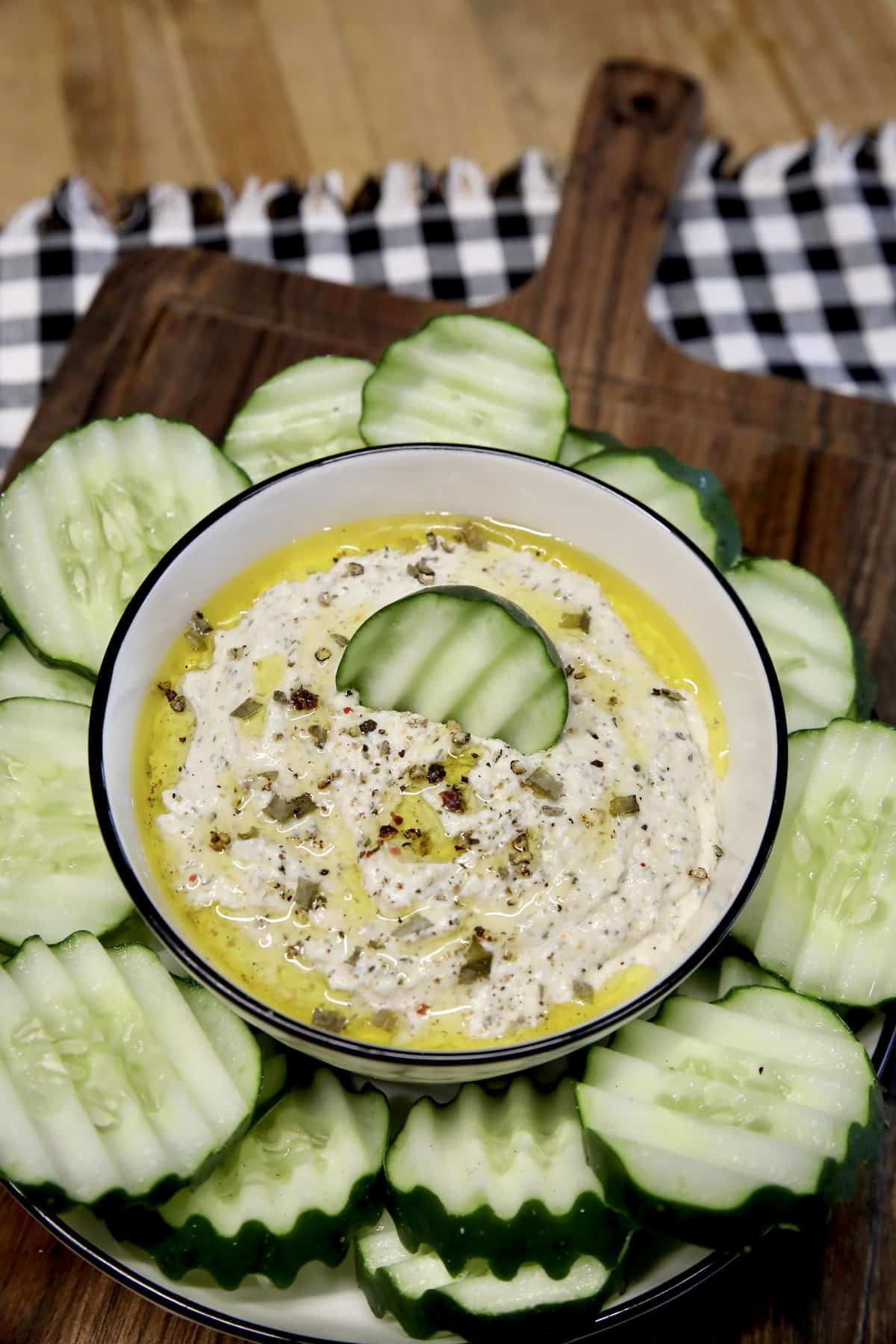 Board with sliced cucumber and bowl of dip.