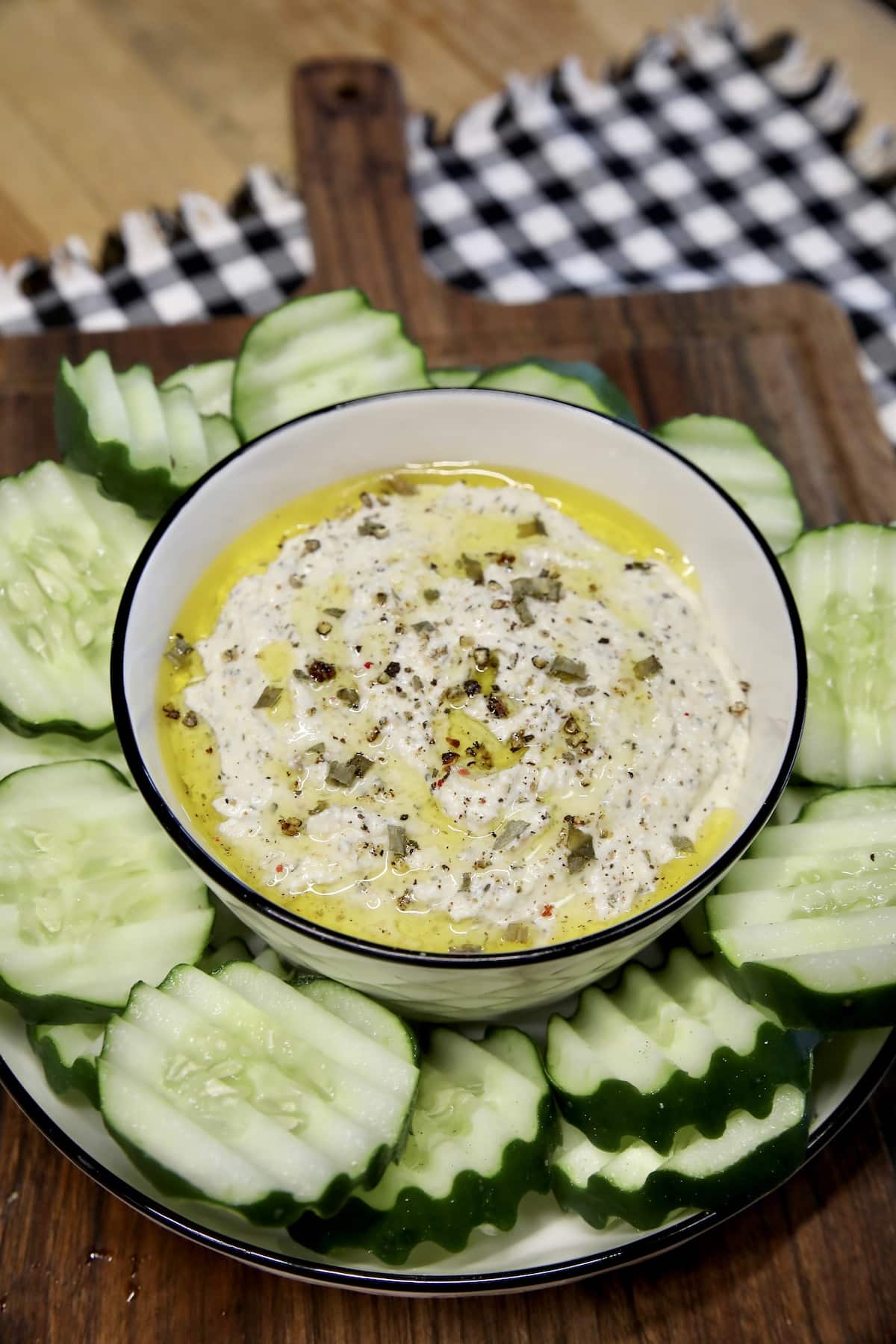 Cottage cheese dip with sliced cucumbers on a board.