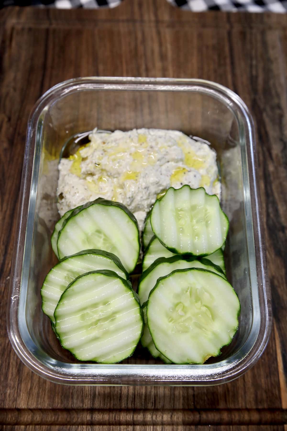 Glass container with sliced cucumbers and dip.