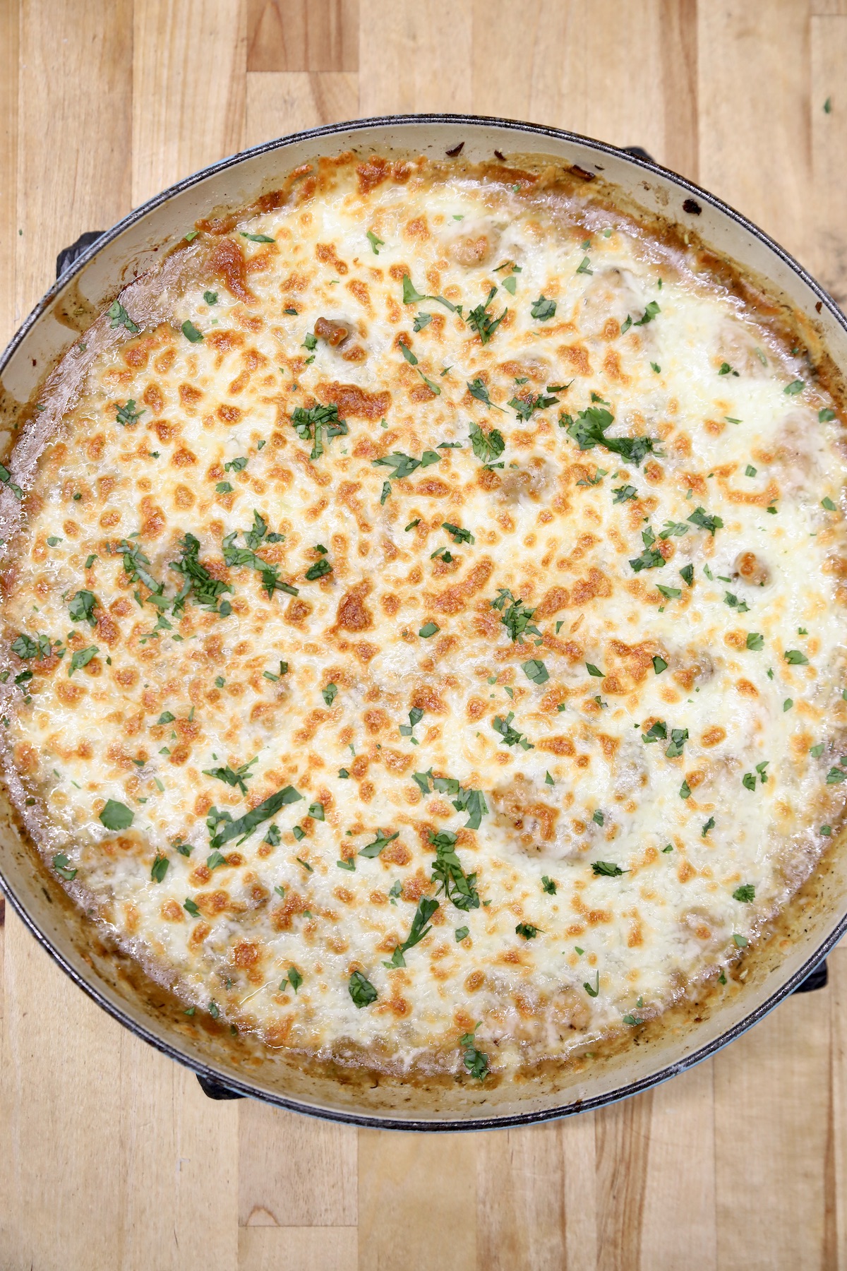 Skillet of French onion chicken with melted cheese and parsley.