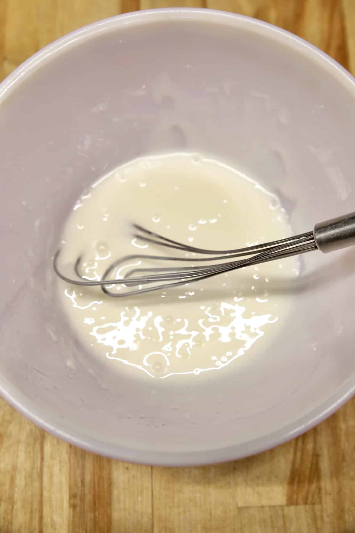 Bowl of powdered sugar icing with whisk.