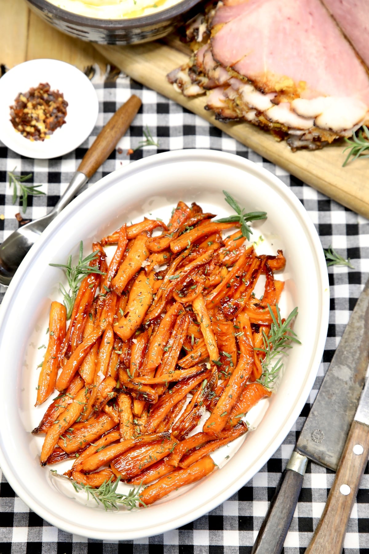 Maple glazed carrots on a platter with ham in background.